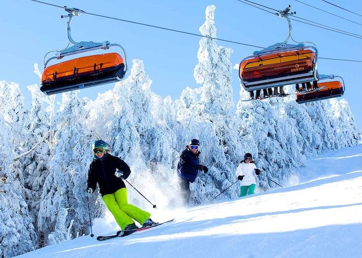 Three skiiers going down a mountain with Okemo branded ski lifts above them