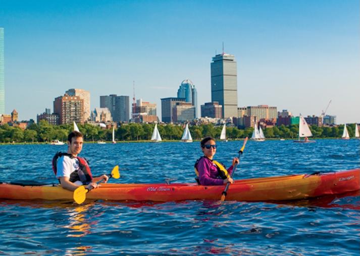 Two people in life vests paddle a kayak on the Charles River